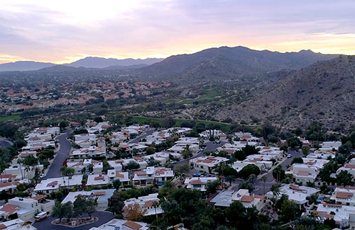 Aerial shot of white and adobe brick community against mountains at sunset
